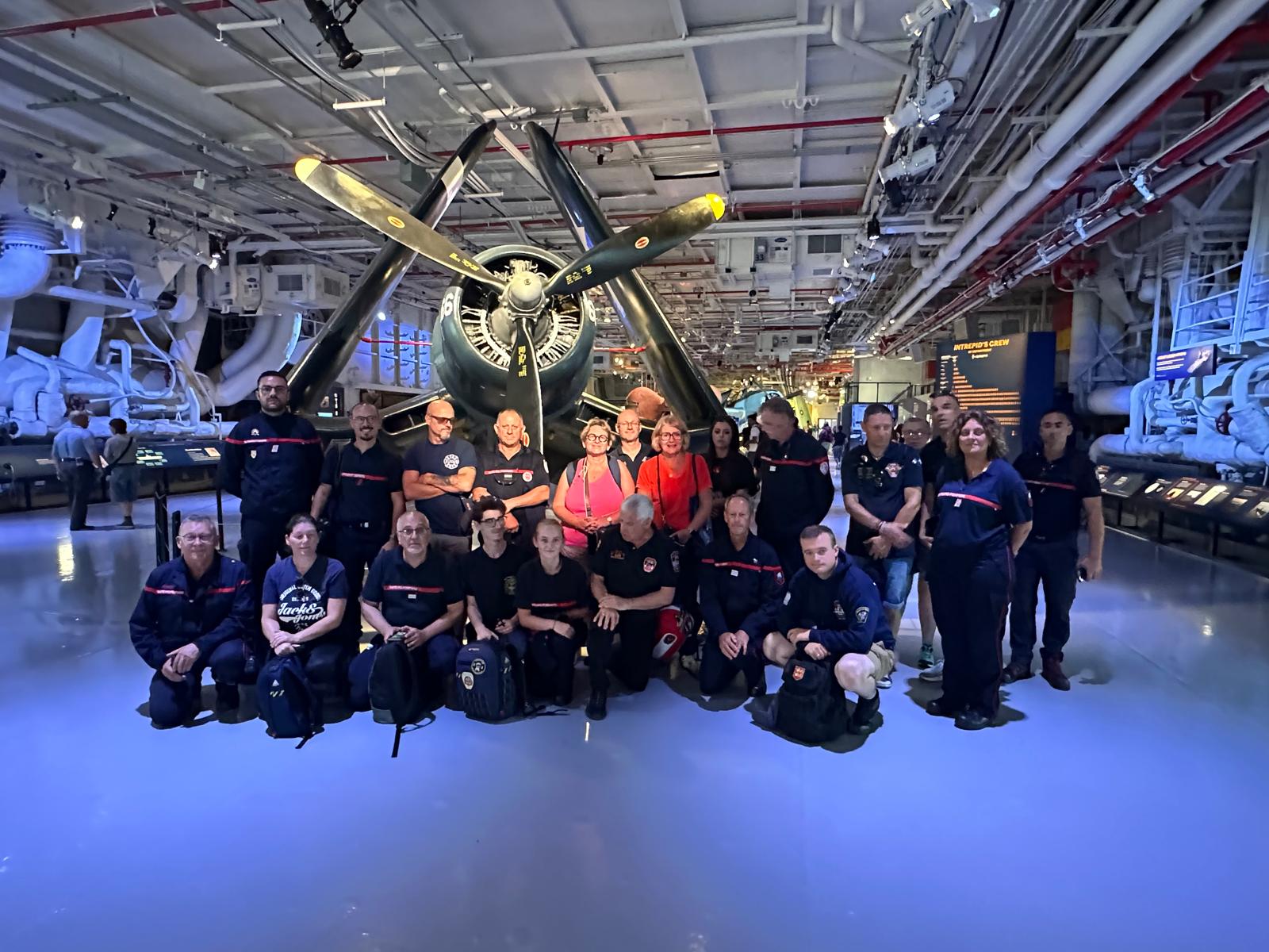 Le groupe de pompiers français au musée du port avion l'Intrepid sea Air Space - En fond un Corsair de la Seconde Guerre Mondiale